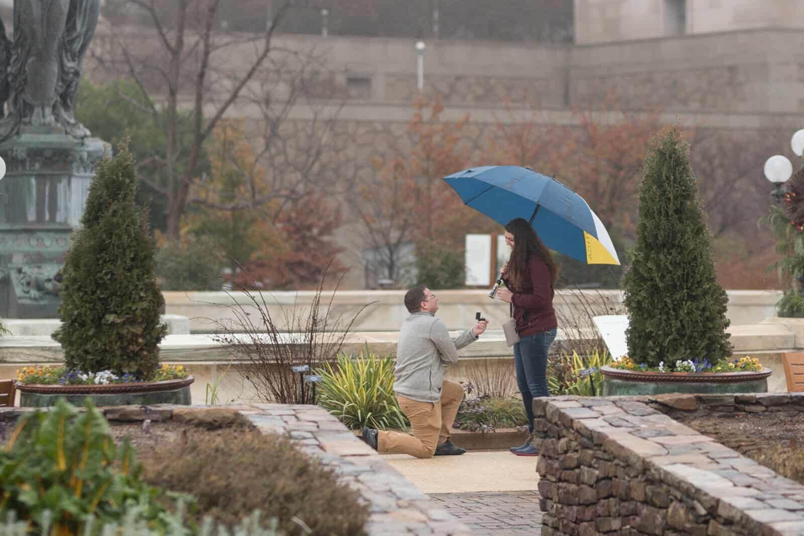 image of man proposing to his girlfriend in the rain in DC in front of the Bartholdi Fountain.