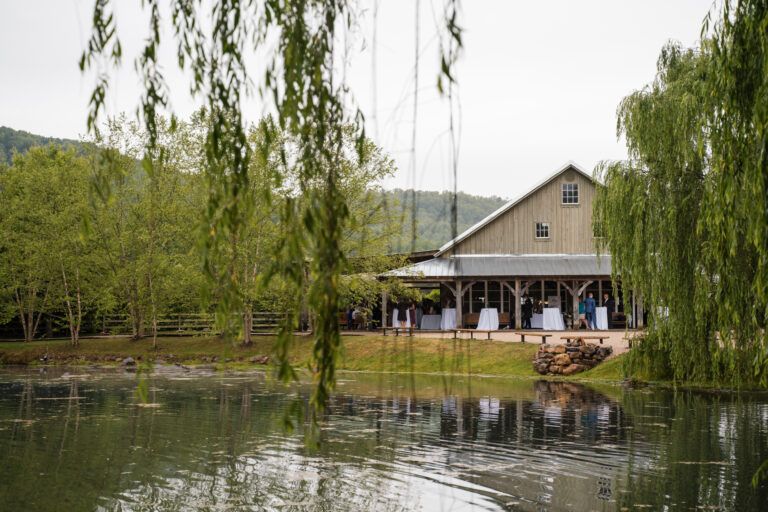View of the barn at Big Spring Farm wedding venue through the willow trees across the pond in Lexington, VA