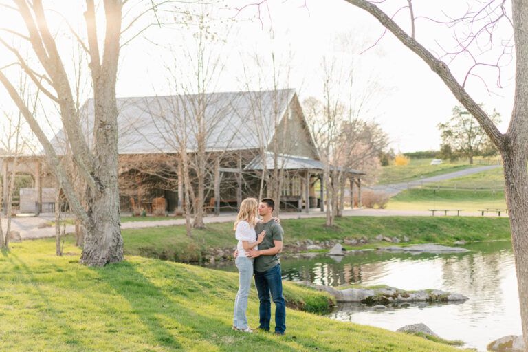 Couple poses for engagement photos at sunset by the lake at Big Spring Farm