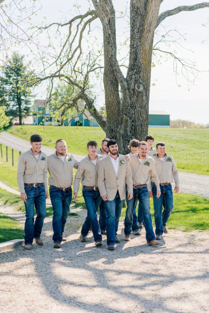 Groomsmen in jeans and tan jackets walking in front of the barn at Sky Ridge Farm, a barn wedding venue in Waynesboro, VA, near the Blue Ridge Mountains. Photo by Wedding Phootography by Jo Mahaney, a Virginia wedding photographer.