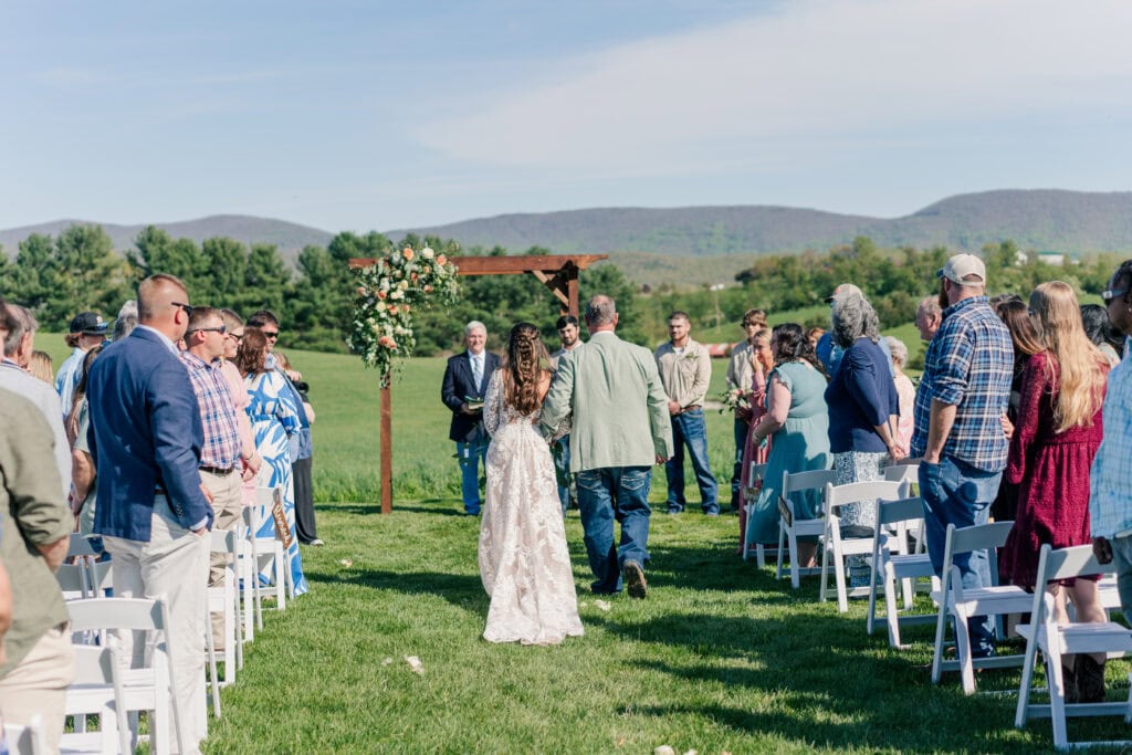 Bride walking down the aisle beside her father at Sky Ridge Farm, a barn wedding venue in Waynesboro, VA, near the Blue Ridge Mountains. Photo by Wedding Phootography by Jo Mahaney, a Virginia wedding photographer.