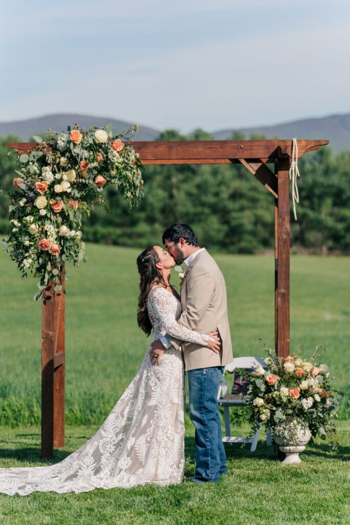 Newlyweds first kiss at Sky Ridge Farm, a barn wedding venue in Waynesboro, VA, near the Blue Ridge Mountains. Photo by Wedding Phootography by Jo Mahaney, a Virginia wedding photographer.