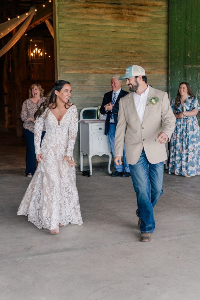 At Sky Ridge Farm, a bride in a lace gown and a groom in a beige jacket and jeans dance joyfully. Guests watch and smile, adding warmth to the enchanting wedding venue.
