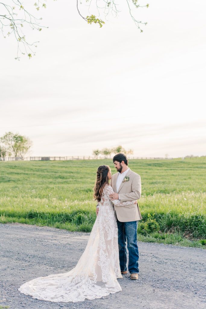 Bride and groom stand facing each other on a gravel path at Sky Ridge Farm, with a grassy field in the background.