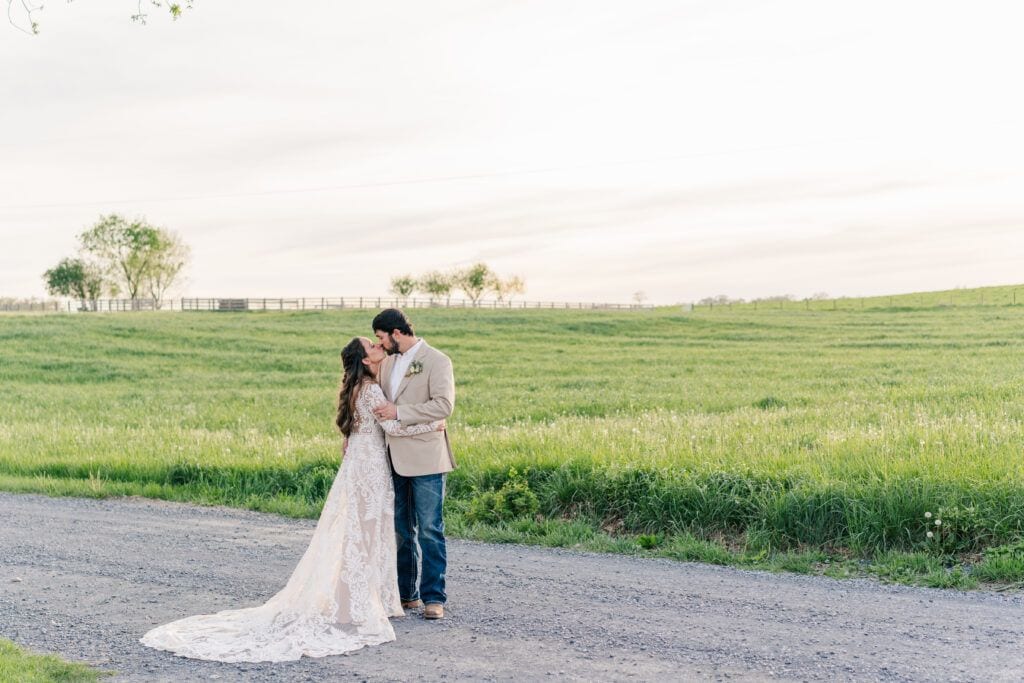 Couple shares a kiss at golden hour in the field at sunset at Sky Ridge Farm, a barn wedding venue in Waynesboro, VA, near the Blue Ridge Mountains. Photo by Wedding Phootography by Jo Mahaney, a Virginia wedding photographer.