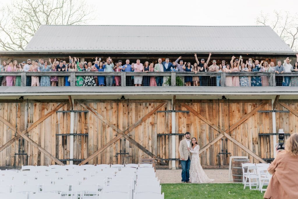 Couple poses in front of all their wedding guests, watching from the balcony above them in the barn at Sky Ridge Farm, a barn wedding venue in Waynesboro, VA, near the Blue Ridge Mountains. Photo by Wedding Phootography by Jo Mahaney, a Virginia wedding photographer.
