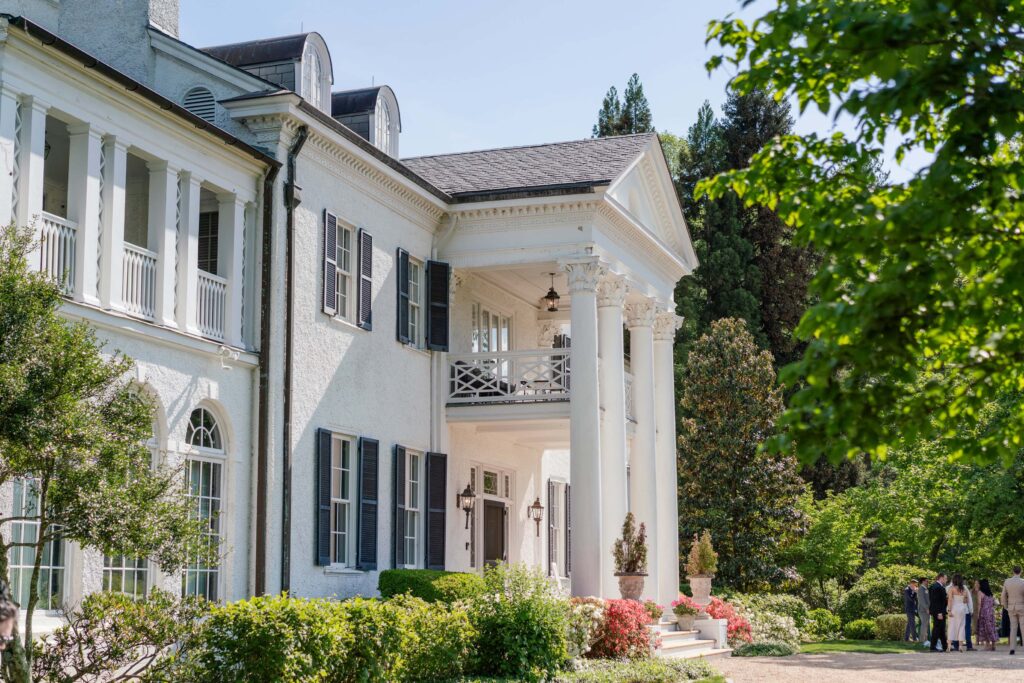A large white mansion with tall columns, black shutters, and a well-maintained garden in front, Keswick Vineyards is the perfect wedding venue under a clear blue sky.