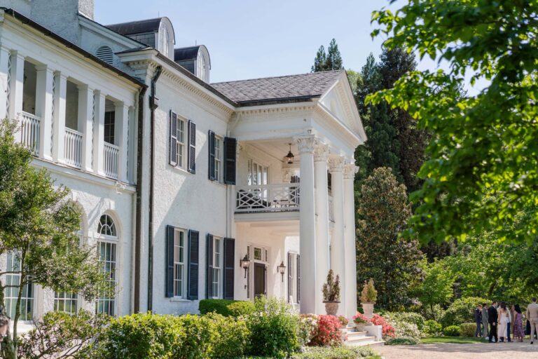 A large white mansion with tall columns, black shutters, and a well-maintained garden in front, Keswick Vineyards is the perfect wedding venue under a clear blue sky.